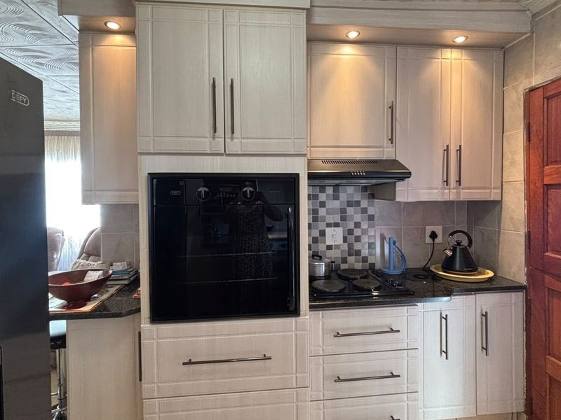 A functional kitchen featuring light-toned cabinetry, granite countertops, a built-in oven, and a tiled backsplash with integrated lighting.