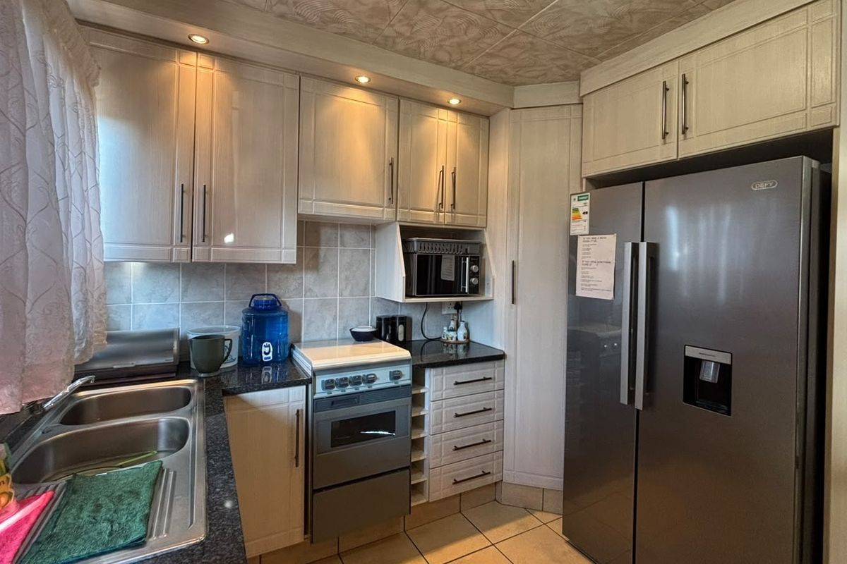 A functional kitchen featuring light-toned cabinetry, granite countertops, a double basin sink, and a tiled backsplash with integrated oven and microwave.