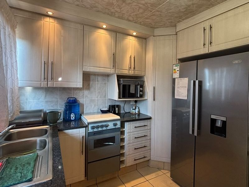 A functional kitchen featuring light-toned cabinetry, granite countertops, a double basin sink, and a tiled backsplash with integrated oven and microwave.