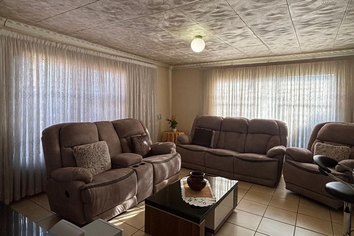 A living room featuring textured ceiling tiles and ceramic floor tiling, offering a dated but functional space ready for modernization.