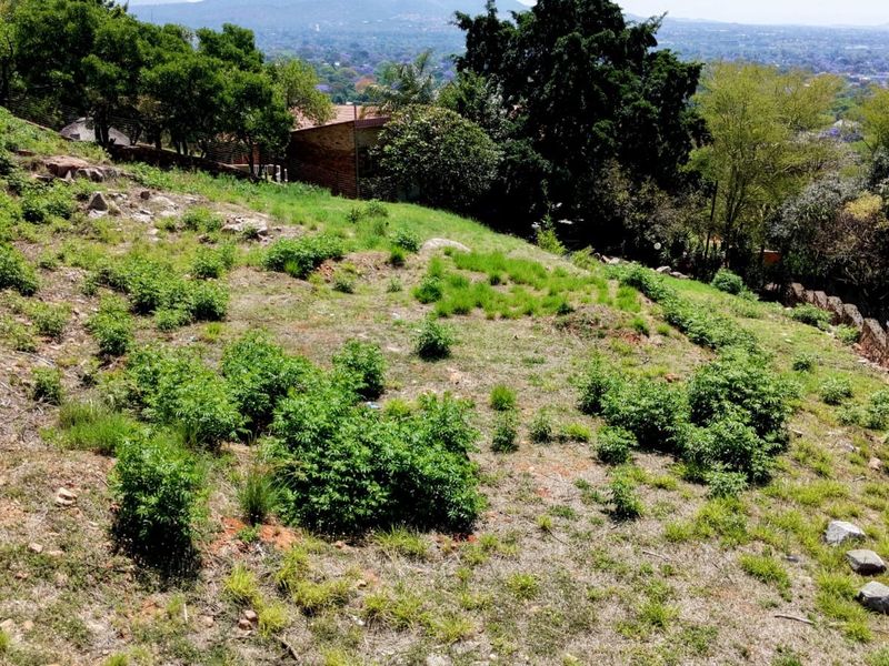 A sloped residential vacant land plot featuring natural vegetation and stone boundary walls with scenic elevated views.