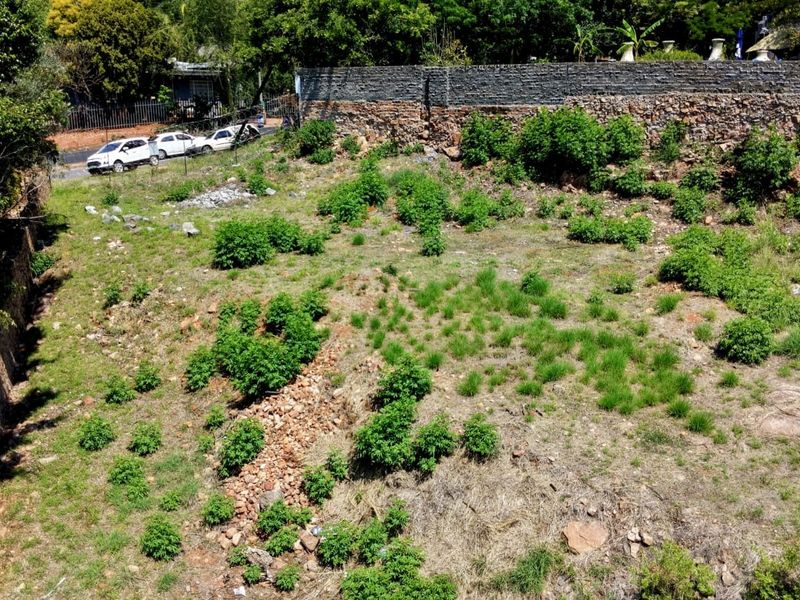 A vacant residential plot featuring a stone boundary wall and natural terrain, offering potential for development in a established neighborhood.
