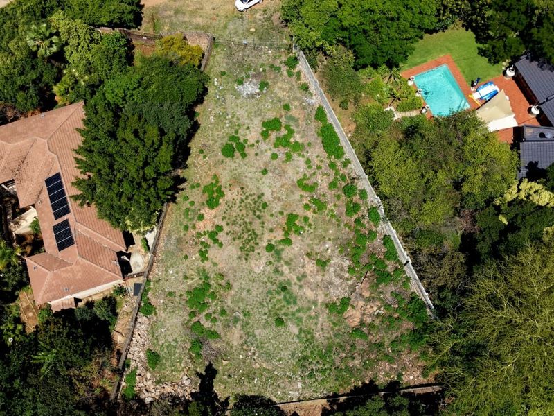 Aerial view of a vacant residential plot situated between established properties, featuring mature trees and existing boundary fencing.