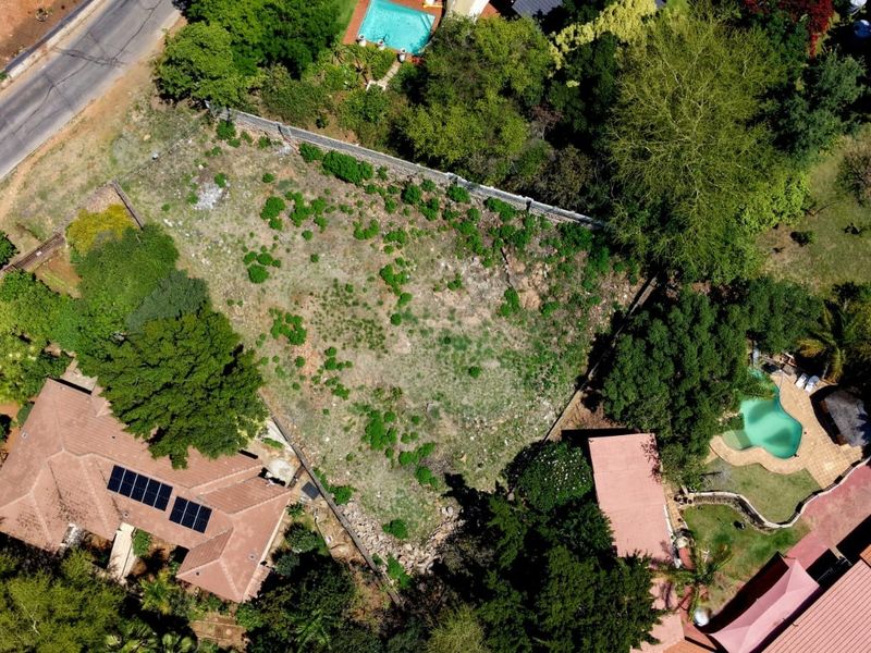 Aerial view of a vacant residential plot surrounded by established trees and neighbouring properties.