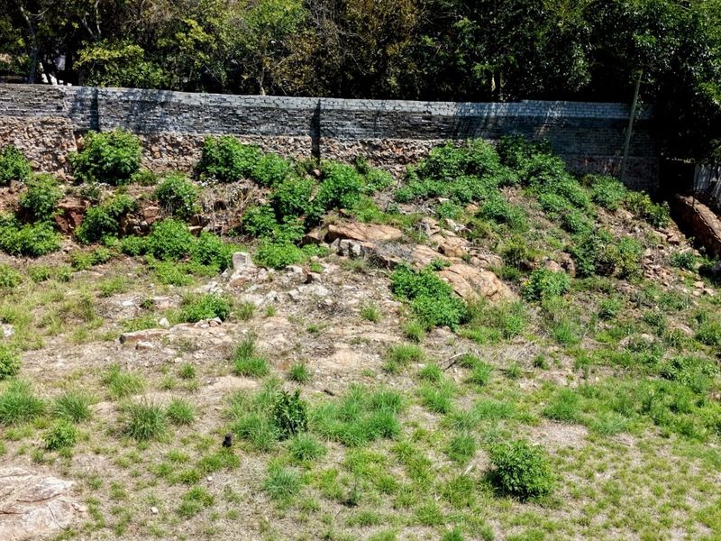 A sloped residential plot featuring natural rocky terrain and a stone retaining wall at the rear boundary.