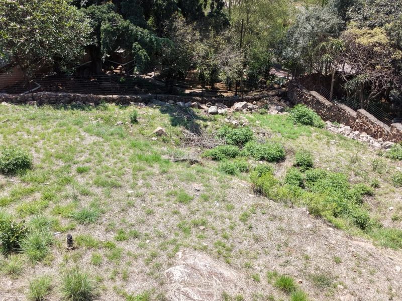 A sloped residential plot featuring natural vegetation, a stone retaining wall, and perimeter fencing, offering potential for landscaping or development.