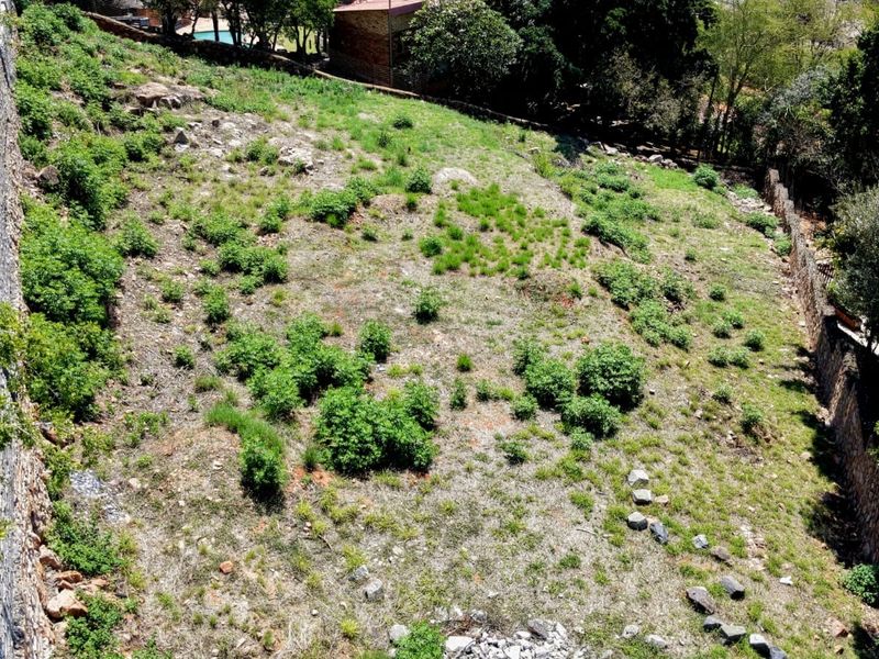 An aerial view of a vacant residential plot featuring natural sloped terrain and established stone retaining walls along the perimeter.
