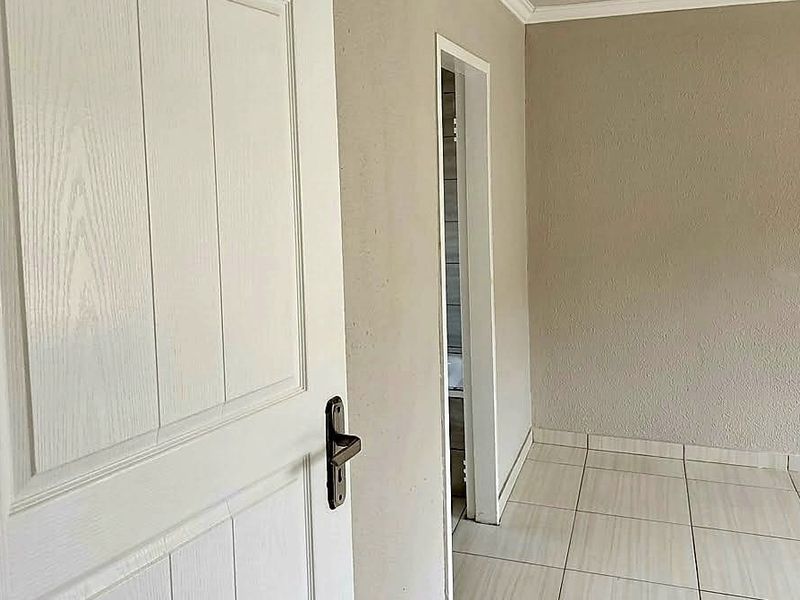 A clean, empty hallway featuring neutral wall tones and light-colored floor tiles, providing a simple transition between rooms.