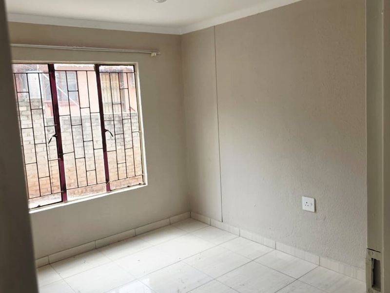 An empty bedroom featuring tiled flooring, neutral walls, and a window fitted with security bars.