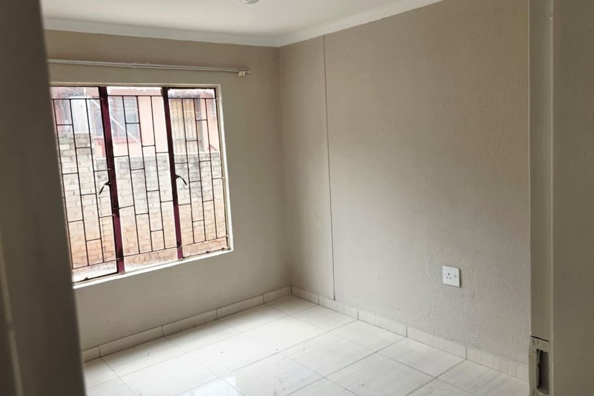 An empty bedroom featuring tiled flooring, neutral walls, and a window fitted with security bars.