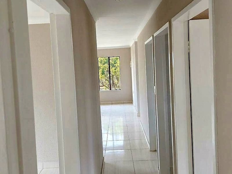 A bright, empty hallway featuring neutral wall finishes and tiled flooring, providing access to multiple rooms within the property.