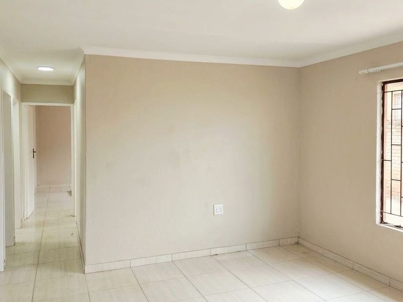 A bright, empty living area featuring neutral wall tones, tiled flooring, and large windows fitted with security bars.