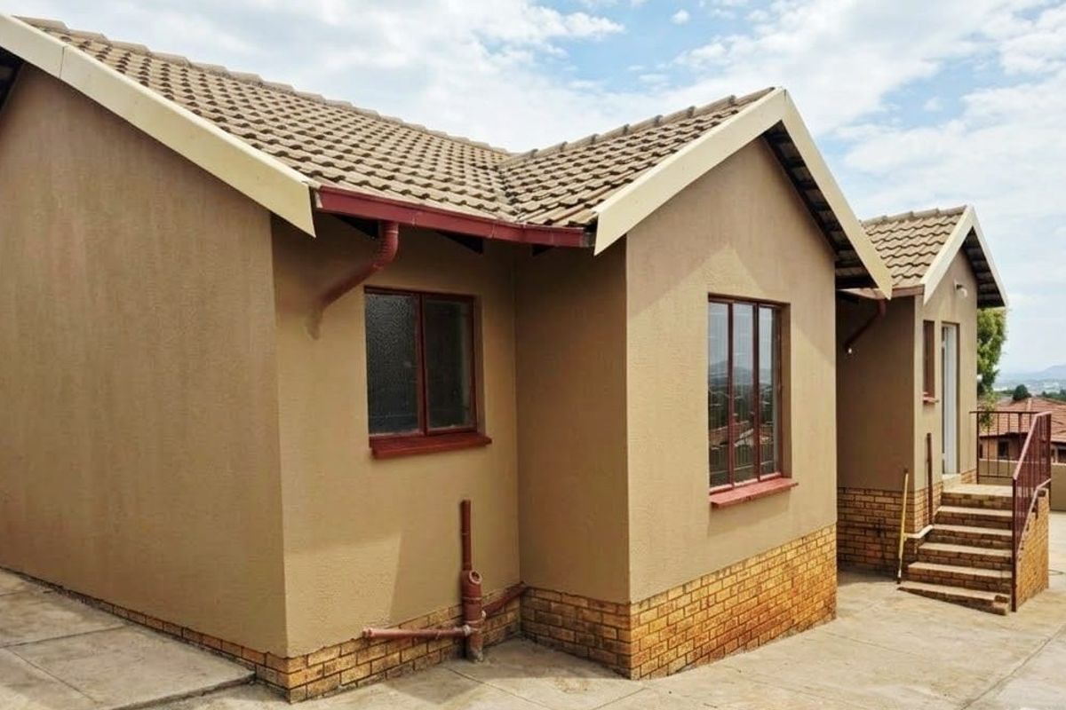 Rear view of a residential house featuring a tiled roof, brick plinth, and concrete paved area with external staircase access.