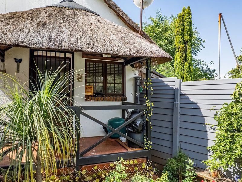 A covered patio area featuring a traditional thatched roof, timber decking, and a security gate, providing a rustic outdoor space.