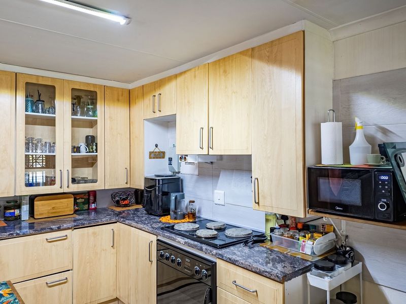 Functional kitchen featuring light wood-finish cabinetry, dark laminate countertops, built-in oven, electric hob, and tiled backsplash with ample storage space.