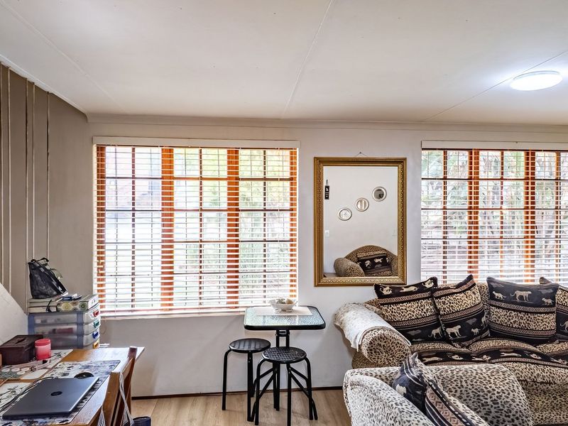 A living room area featuring laminate flooring, wooden venetian blinds, and a staircase railing, offering a functional space with potential for cosmetic updates.