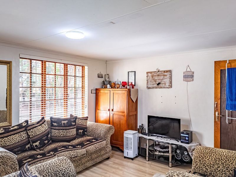 A living room featuring laminate flooring and venetian blinds, showing signs of wear including ceiling cracks and wall imperfections.