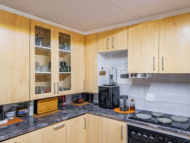 A functional kitchen featuring light wood-finish cabinetry, dark laminate countertops, a tiled backsplash, and a built-in electric hob and oven.