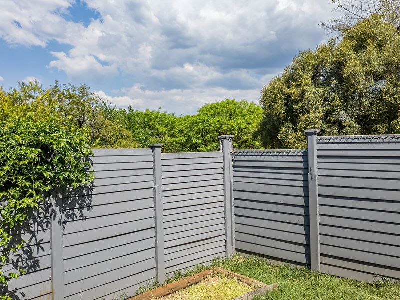 A private rear garden area featuring grey timber slat fencing and a raised garden bed, set against a backdrop of mature trees.