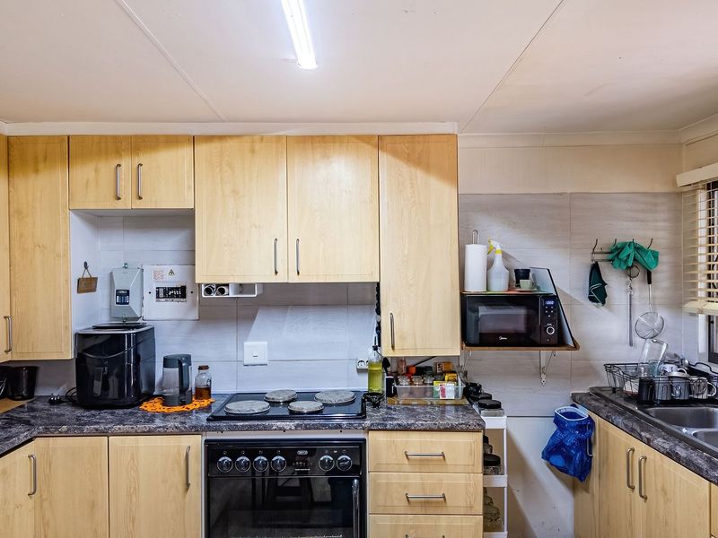 A functional kitchen featuring light wood-tone cabinetry, laminate countertops, a built-in oven with electric hob, and a double stainless steel sink.