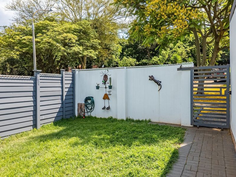 A private rear garden area featuring a well-maintained lawn, paved walkway, and secure perimeter fencing with a metal gate.