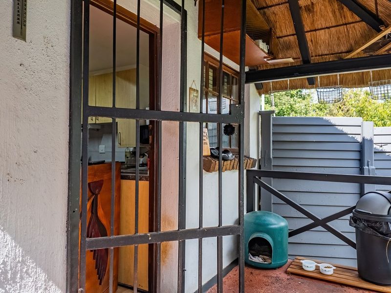 Covered patio area featuring a thatched roof, timber railing, and a security gate, providing direct access to the interior kitchen space.