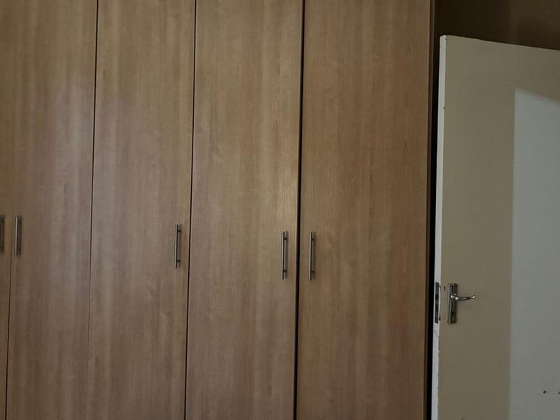 A bedroom featuring wood-finish built-in cupboards and a standard internal door, providing functional storage space.