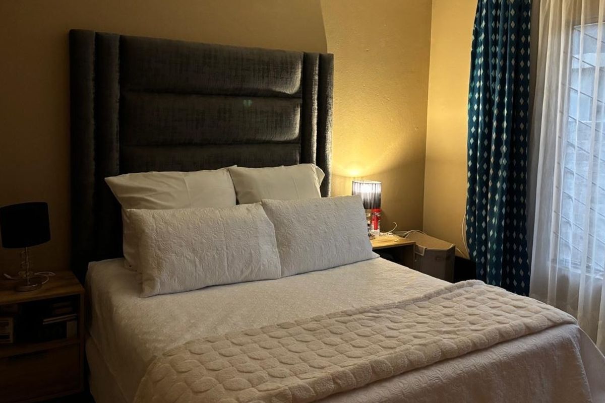 A cozy bedroom featuring a large upholstered headboard, neutral wall tones, and window treatments providing natural light.