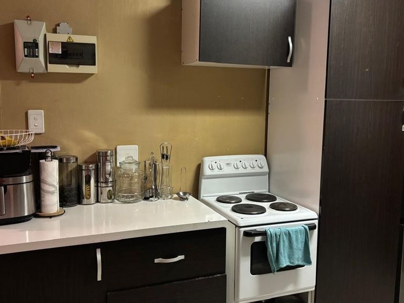 A compact kitchen area featuring dark cabinetry, a white countertop, and a freestanding electric stove.