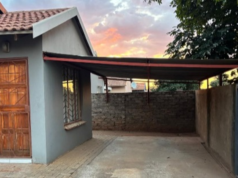 Front exterior view of the property featuring a paved driveway, a covered carport, and a secure entrance with a metal security gate.