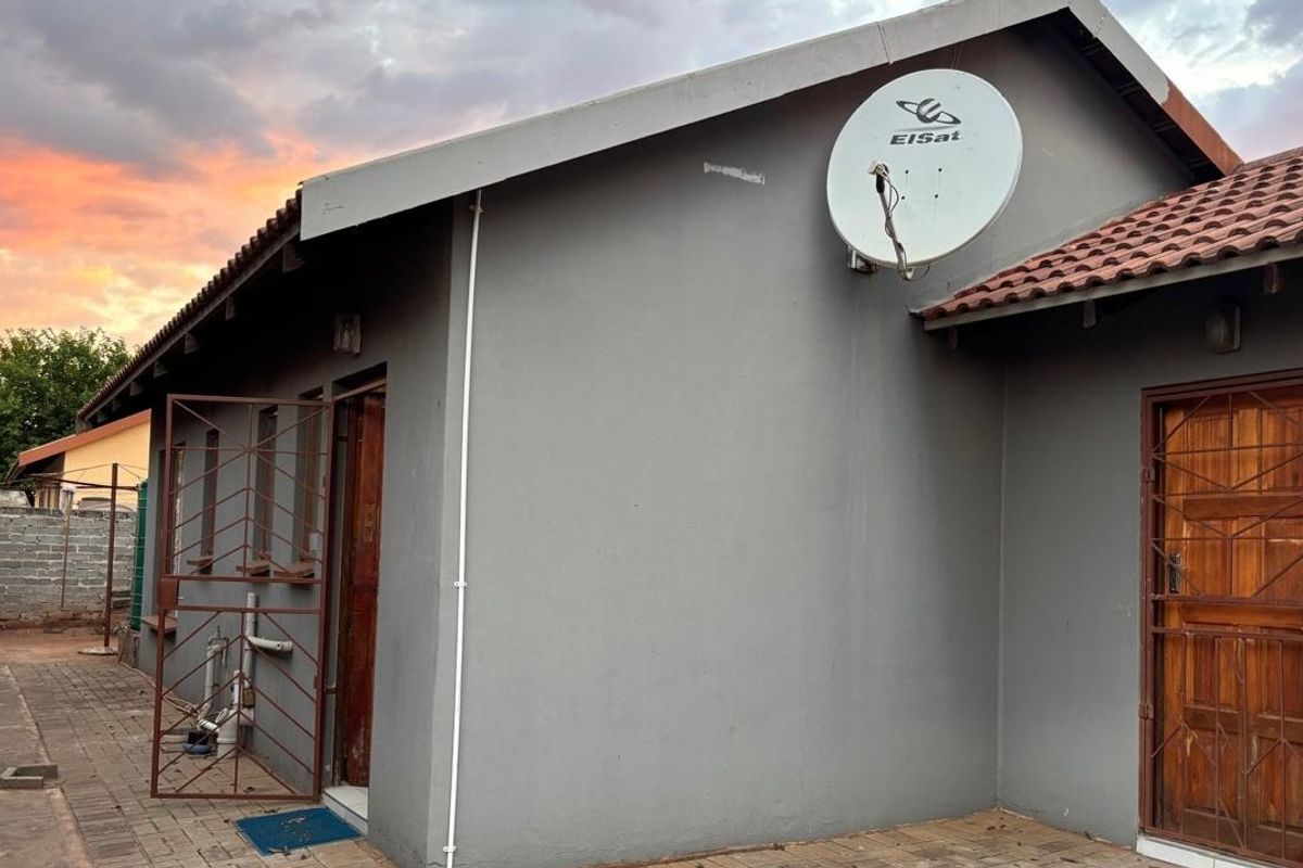 Rear exterior view of the house featuring a paved patio area, security gates on doors, and a satellite dish mounted on the wall.