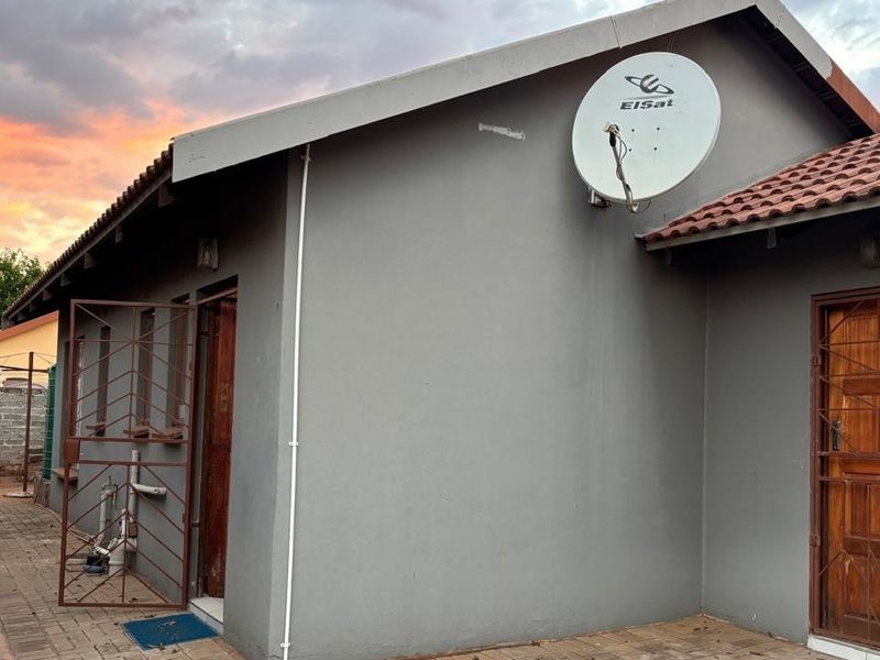 Rear exterior view of the house featuring a paved patio area, security gates on doors, and a satellite dish mounted on the wall.
