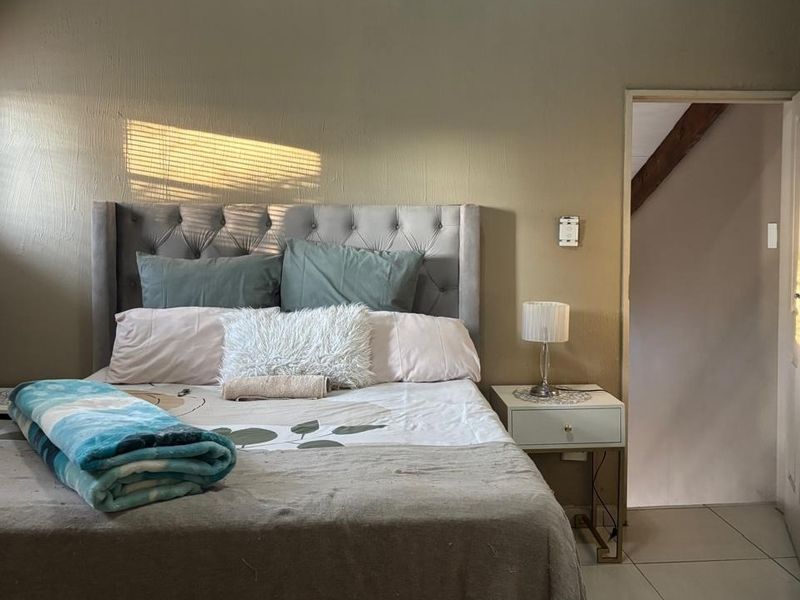 A bedroom featuring tiled flooring, built-in cupboards, and venetian blinds, with natural light entering from the side window.