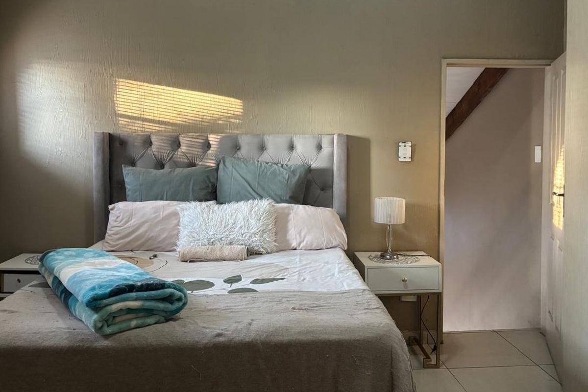 A bedroom featuring tiled flooring, built-in cupboards, and venetian blinds, with natural light entering from the side window.