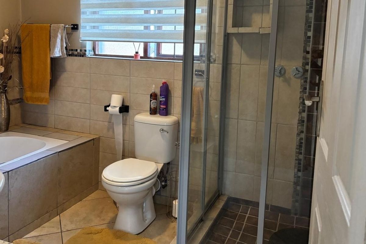 A functional bathroom featuring a built-in bathtub, a separate glass-enclosed shower, a toilet, and a basin with neutral ceramic tiling throughout.