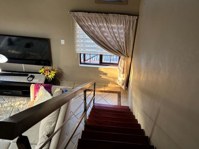 A view looking down a staircase into a living area featuring tiled floors, a metal balustrade, and natural light from the windows.