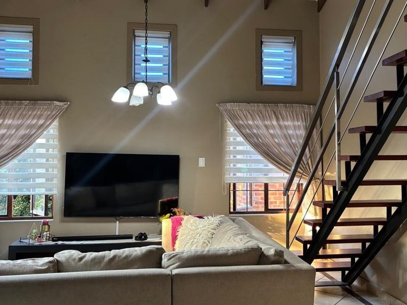 Spacious living room featuring a double volume ceiling with exposed rafters and a modern staircase with timber treads and metal handrails.