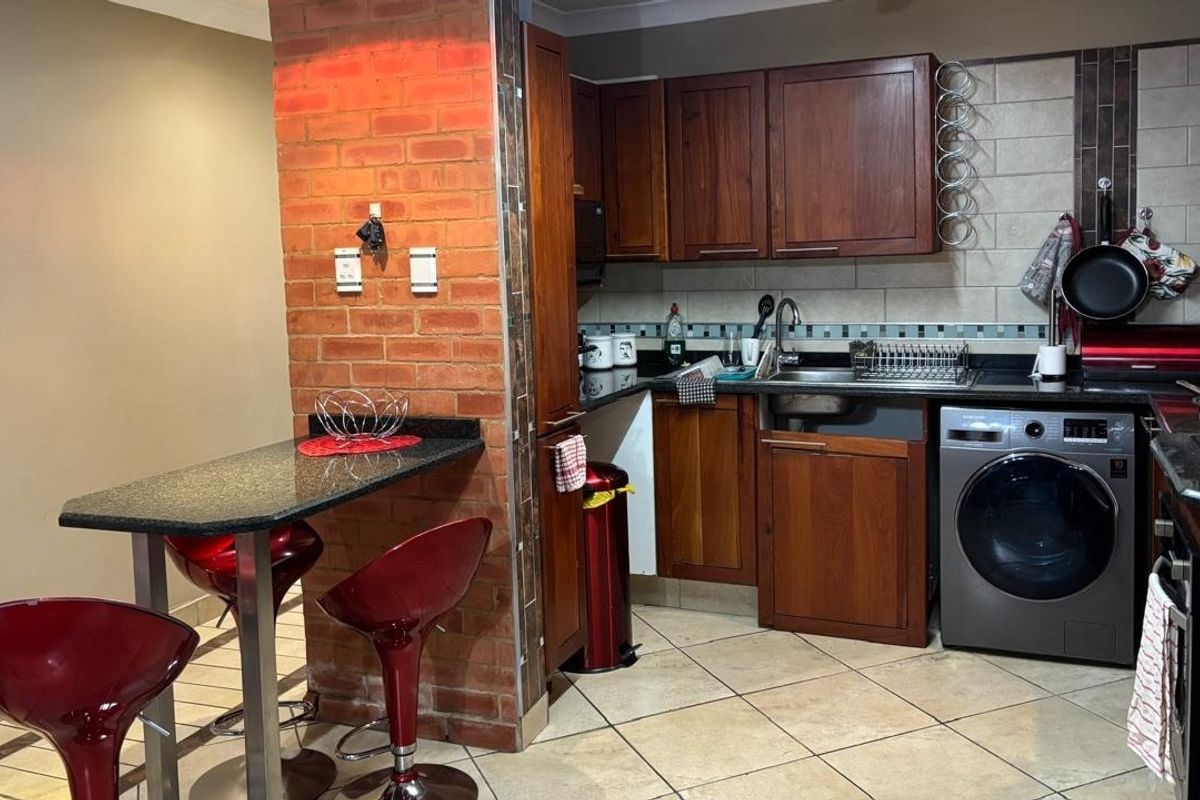 A functional kitchen featuring wooden cabinetry, granite countertops, an exposed brick breakfast bar, and integrated appliances with tiled flooring and backsplash.