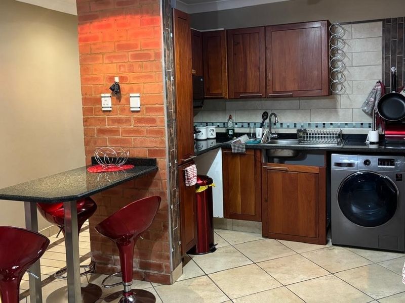 A functional kitchen featuring wooden cabinetry, granite countertops, an exposed brick breakfast bar, and integrated appliances with tiled flooring and backsplash.