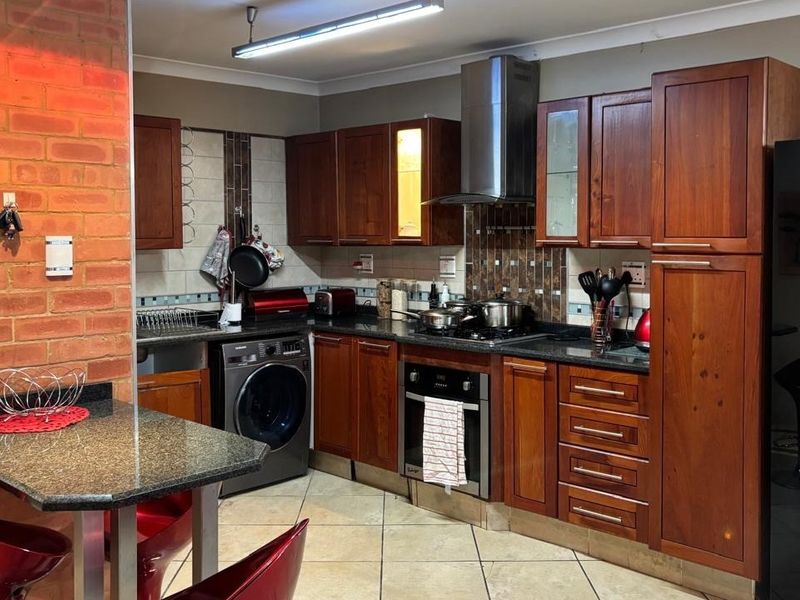 Functional kitchen featuring warm wooden cabinetry, granite countertops, a built-in oven with gas hob, and a distinctive exposed brick feature wall.