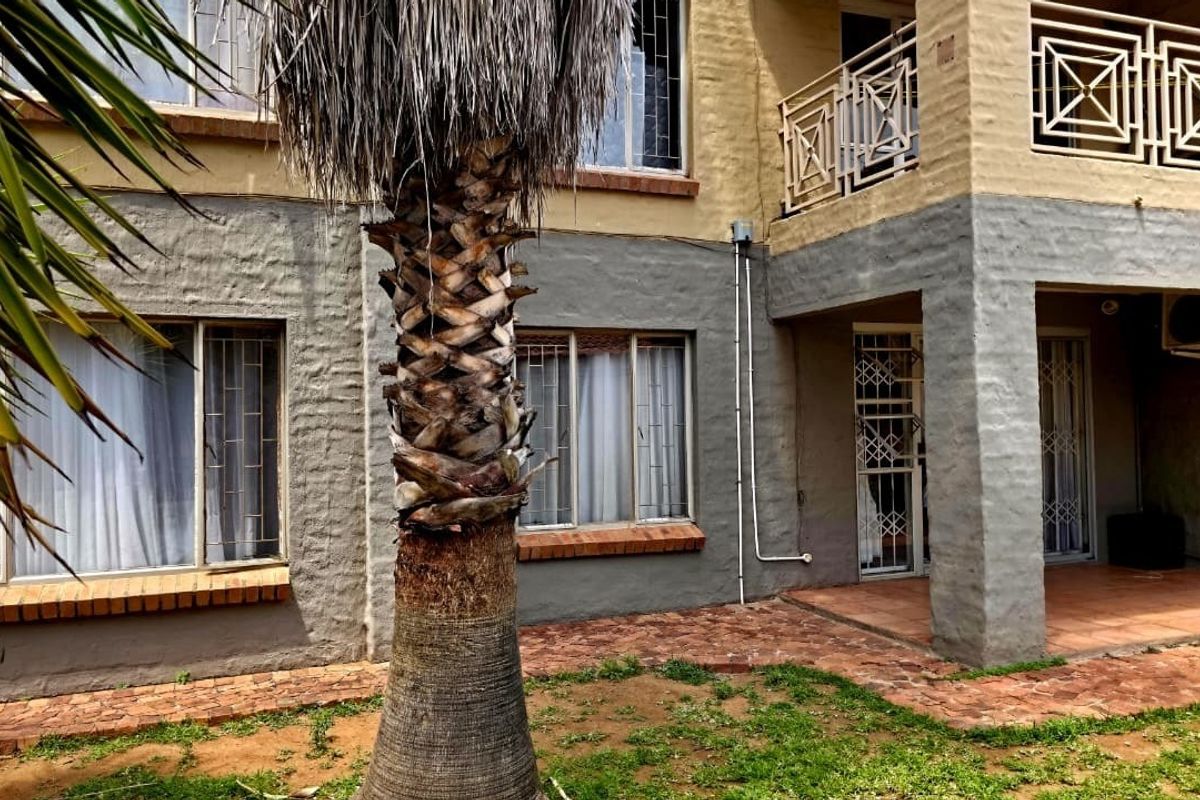 Rear exterior view of the property featuring a brick patio, security bars on windows, and a balcony with metal railing.