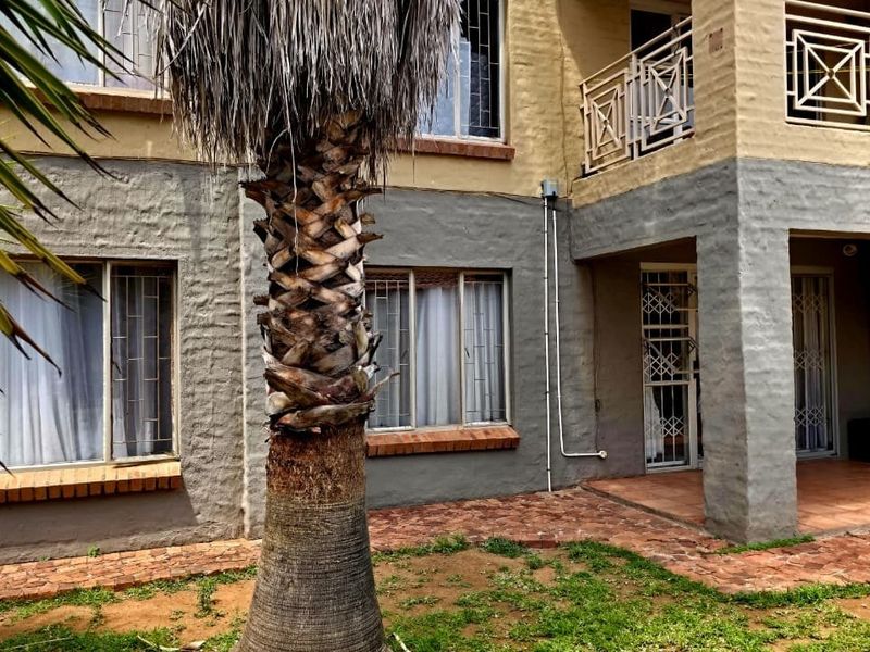 Rear exterior view of the property featuring a brick patio, security bars on windows, and a balcony with metal railing.