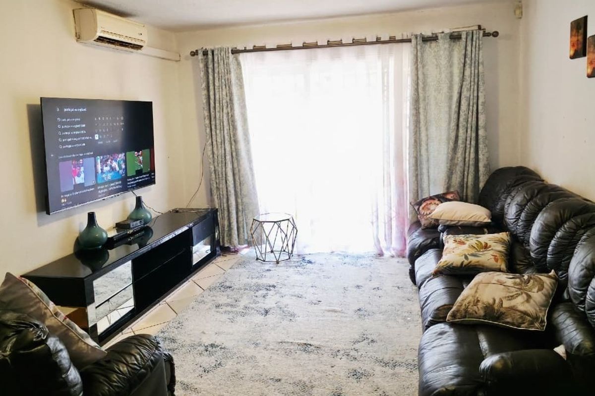A comfortable living room featuring tiled flooring, a wall-mounted air conditioning unit, and a large sliding glass door providing natural light.