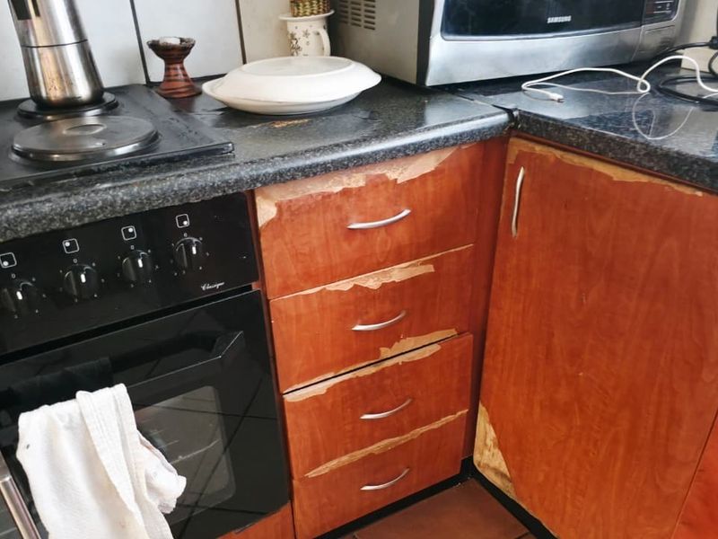 A kitchen area featuring a built-in oven and hob with significant wear and peeling veneer on the cabinetry, indicating a need for refurbishment.