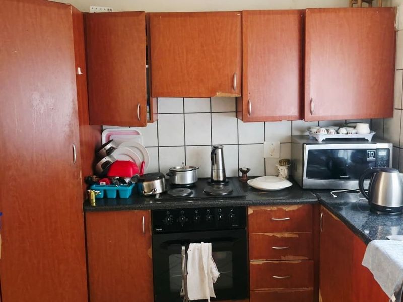 A functional kitchen featuring wood-finish cabinetry, dark laminate countertops, a built-in oven with hob, and tiled backsplash, showing signs of wear on the cabinetry.