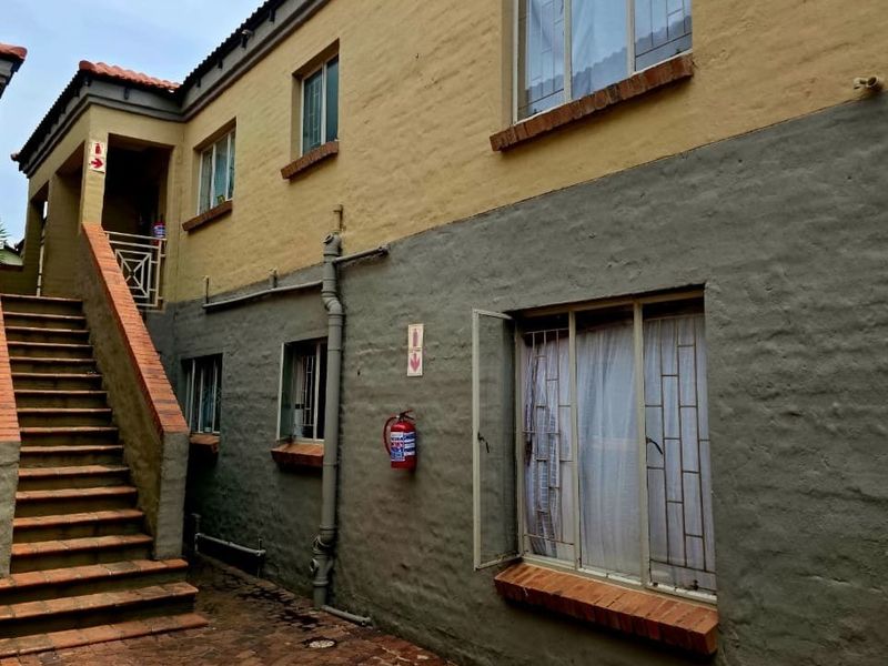 Exterior view of a multi-story residential building featuring a brick staircase, security gates, and functional fire safety equipment.
