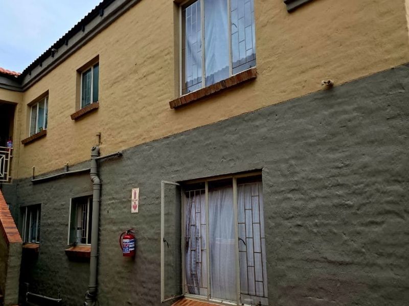 Exterior view of the building featuring a staircase, security bars on windows, and a textured two-tone plaster finish.