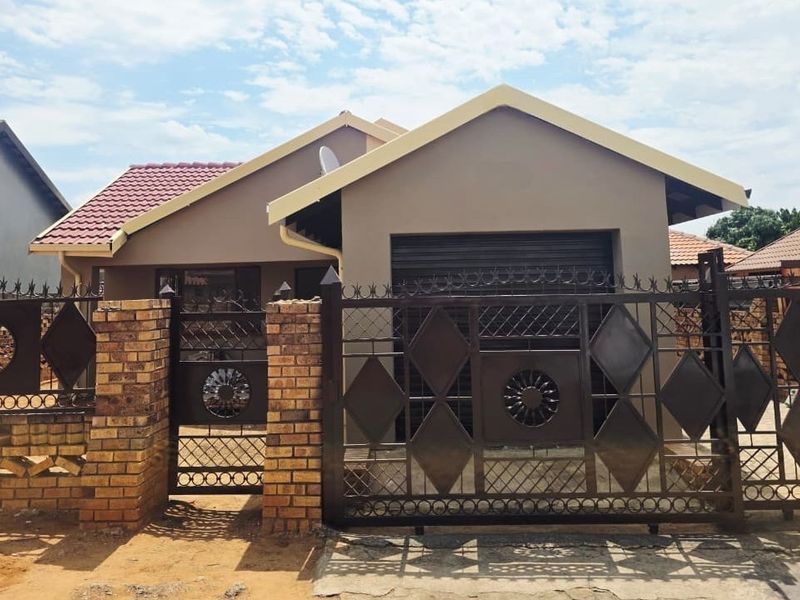 Front view of a single-story residential house featuring a tiled roof, secure metal gate, and brick boundary wall.