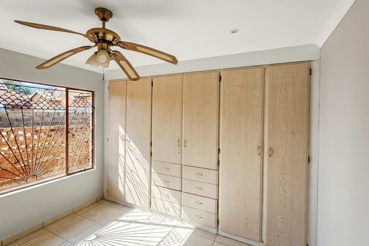 A bright bedroom featuring extensive built-in wooden cabinetry, tiled flooring, and a ceiling fan, offering a clean and functional space.