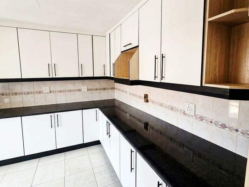 A functional kitchen featuring white built-in cabinetry, dark granite countertops, and a tiled backsplash, offering a clean and practical workspace.